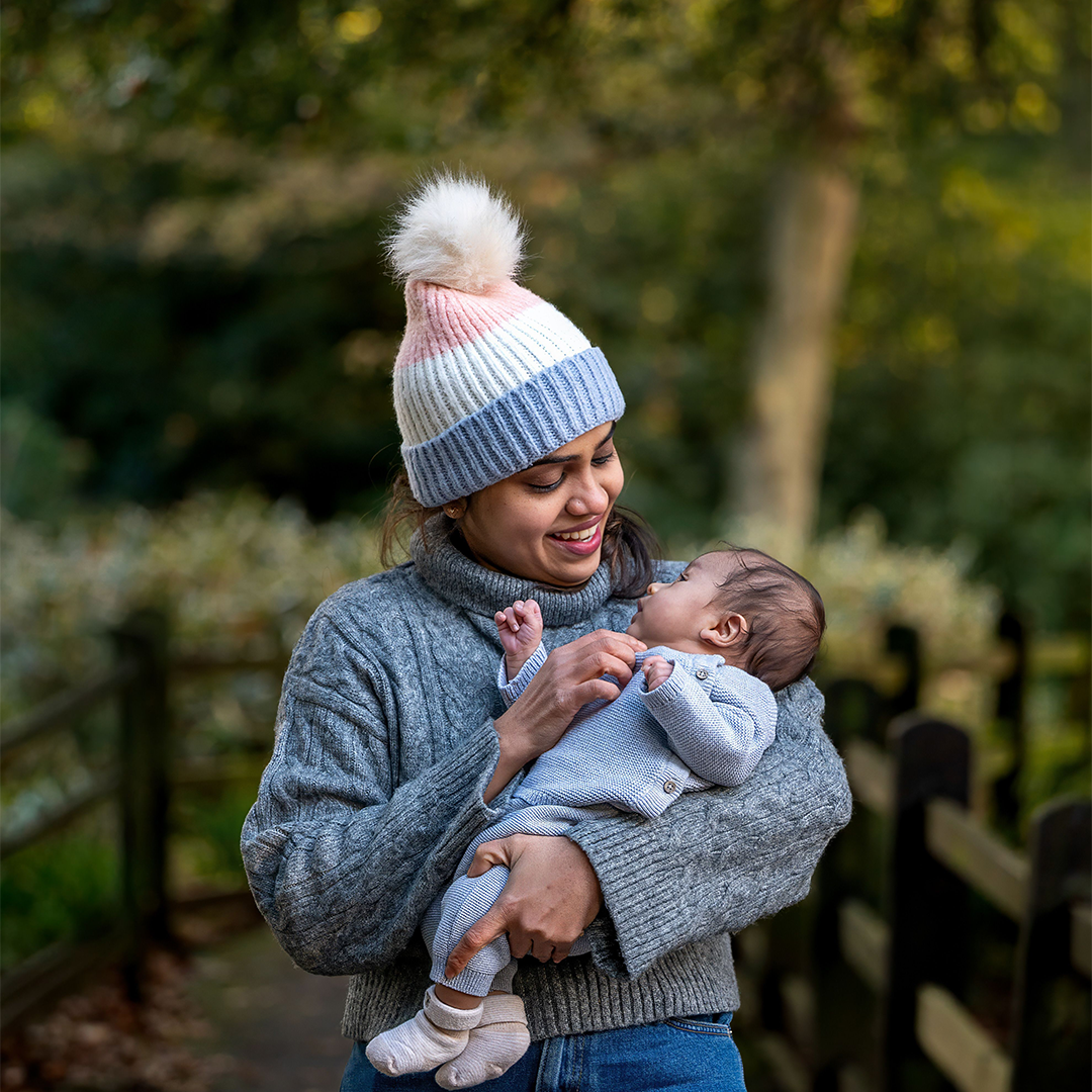 Mother in a knit hat holding her newborn outdoors