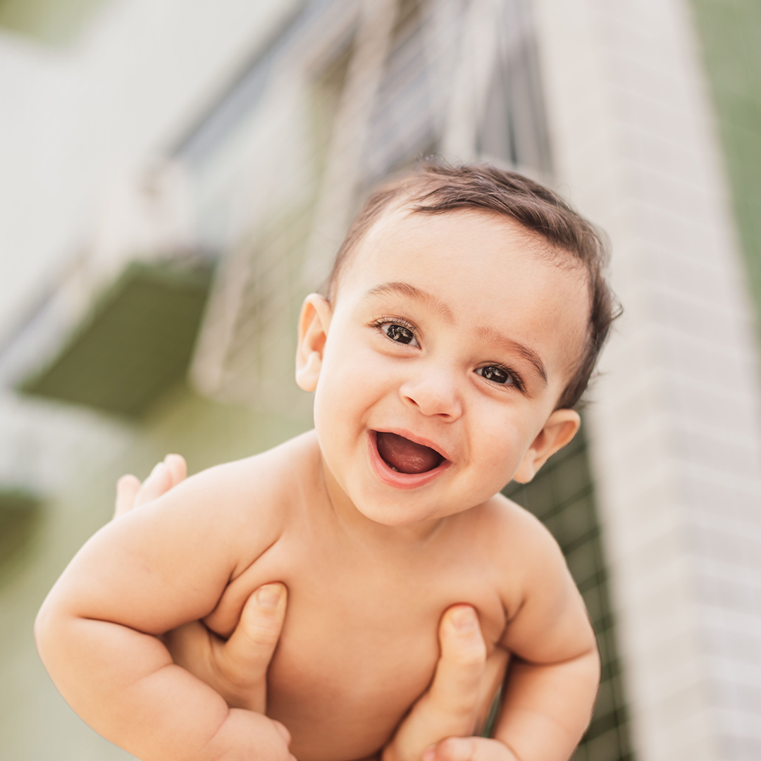 Close-up of a smiling baby held up outdoors